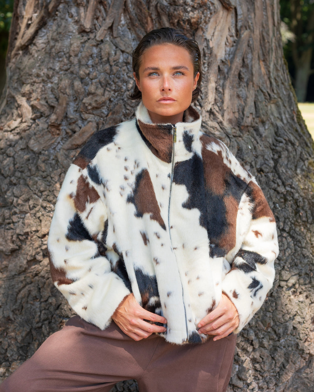 Person wearing a cow patterned jacket standing against a tree